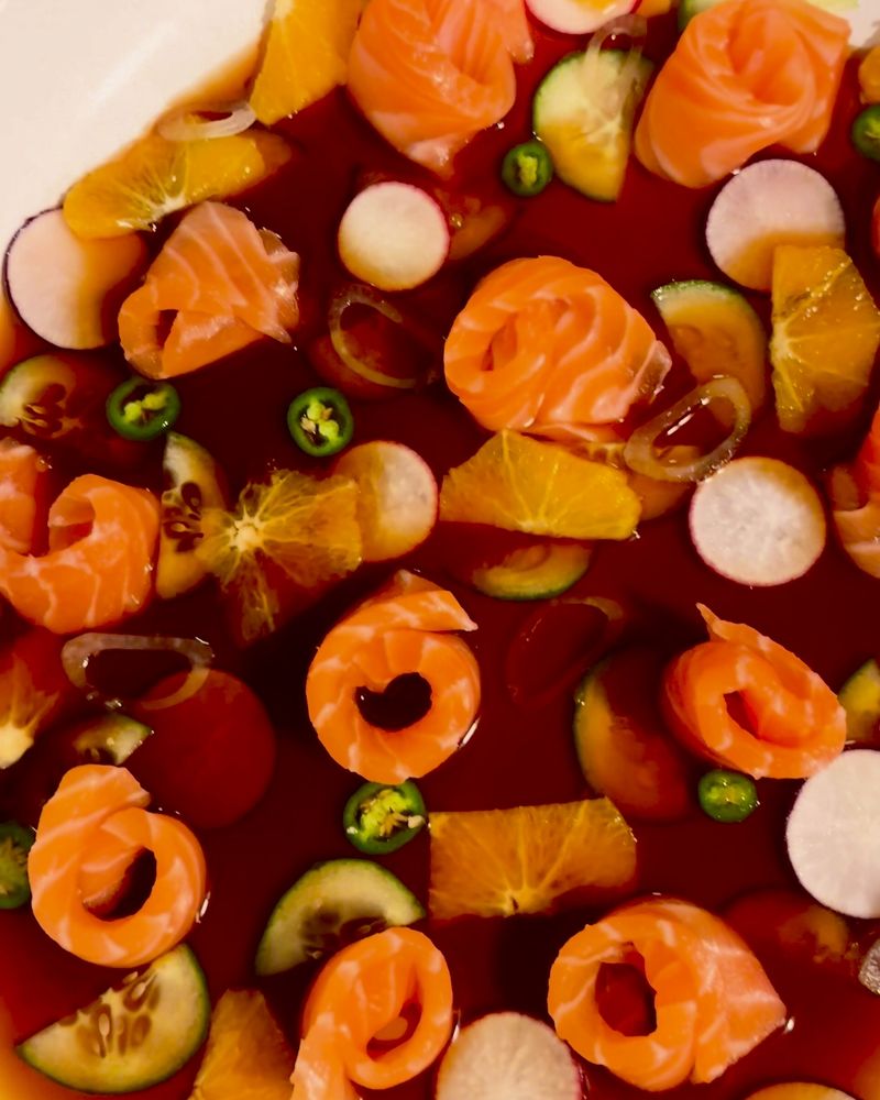 Salmon crudo with orange, cucumber, radish and jalapeño in a shallow pool of sauce.